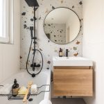 Kúpeľňa s čiernou sprchovacou súpravou, vaňou, umývadlom so skrinkou a terazzom na stene