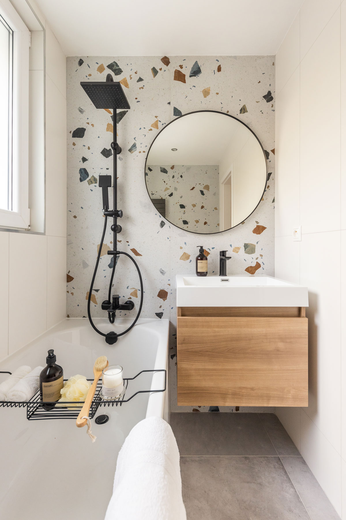 Kúpeľňa s čiernou sprchovacou súpravou, vaňou, umývadlom so skrinkou a terazzom na stene