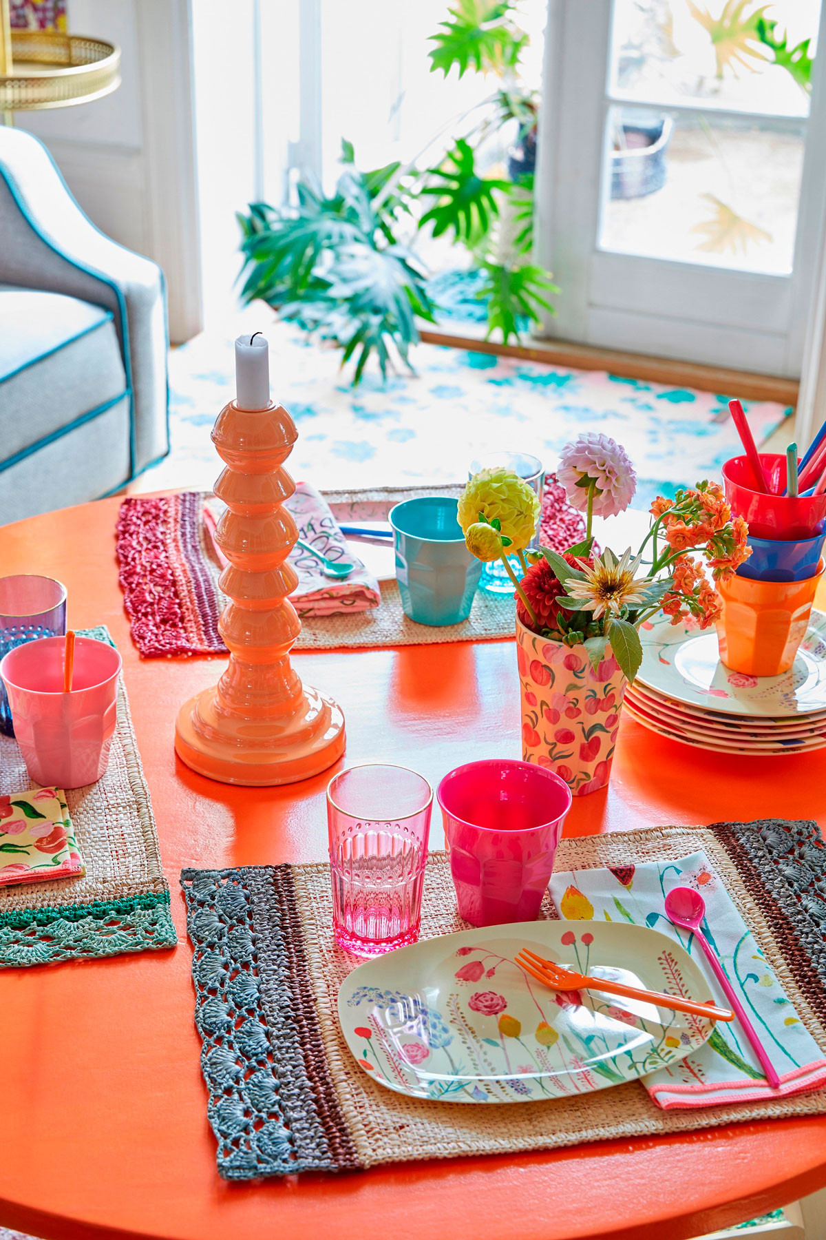 Oranžový stôl s farebným prestieraním, veselými kvetinovými taniermi a rôznofarebnými pohármi