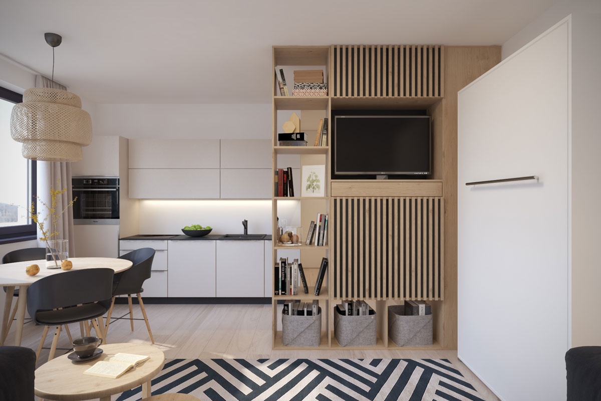 Moderný malý byt s bielou kuchynskou linkou, okrúhlym jedálenským stolom, priestor kuchyne od obývacej časti oddeľuje drevená policová stena, po pravej strane vidieť vyklápaciu posteľ
