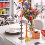 Detail jedálenského stola s vázou s pestrými kvetmi a vtipnými doplnkami, ktoré dotvárajú atmosféru