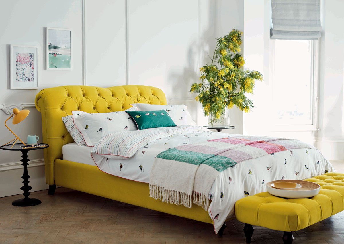 Spálňa s čalúnenou žltou posteľou v klasickom štýle, s vysokým čelom a divánom