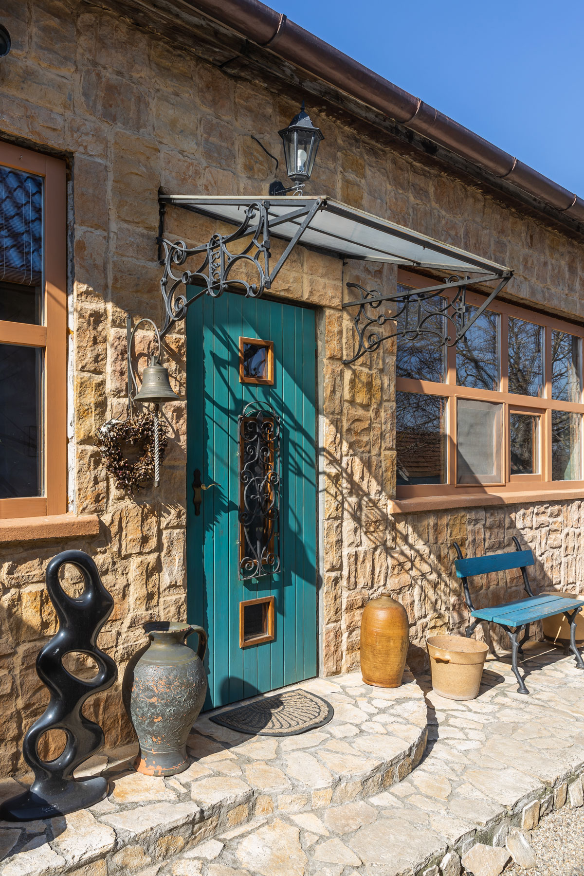 rodinný dom s kamenným obkladom a tyrkysovými vstupnými dverami, exteriér domu je inšpirovaný Balkánom