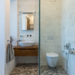 moderná kúpeľňa so sprchovým kútom, závesným WC, svetlým obkladom na stenách a vzorovanou dlažbou, jednoduché umývadlo dopĺňa dubová skrinka