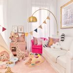 Obývacia časť spojená s detským kútikom, pri stene stojí biela sedačka a ružové kreslo, spoza sedačky vychádza zlatá matná lampa, pri ďalšej stene je kuchynka pre dievčatko a v strede miestnosti sú hračky s típí