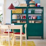 Smaragdovozelené skrinky a stôl so stoličkami zo svetlého dreva na žltom koberci