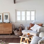 obývačka na chalupe vo vidieckom štýle, dve svetlé pohodlné kreslá dopĺňa prírodný príručný stolík, na drevenej podlahe je nenápadný hnedý koberec, pri stene stojí jednoduchá retro komoda