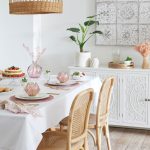Jedáleň v etno štýle s bielou komodou s orientálnou rezbou na dvierkach, vedľa je stôl s drevenými stoličkami s viedenským výpletom, na stole je biely obrus, taniere na ružovom prestieraní a misky v tvare lotosového kvetu