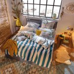 Spálňa so vzorovaným kobercom, čalúnenou posteľou a farebnými modro-bielymi obliečkami so vzorom rastlín z jednej strany a pásikmi z druhej strany