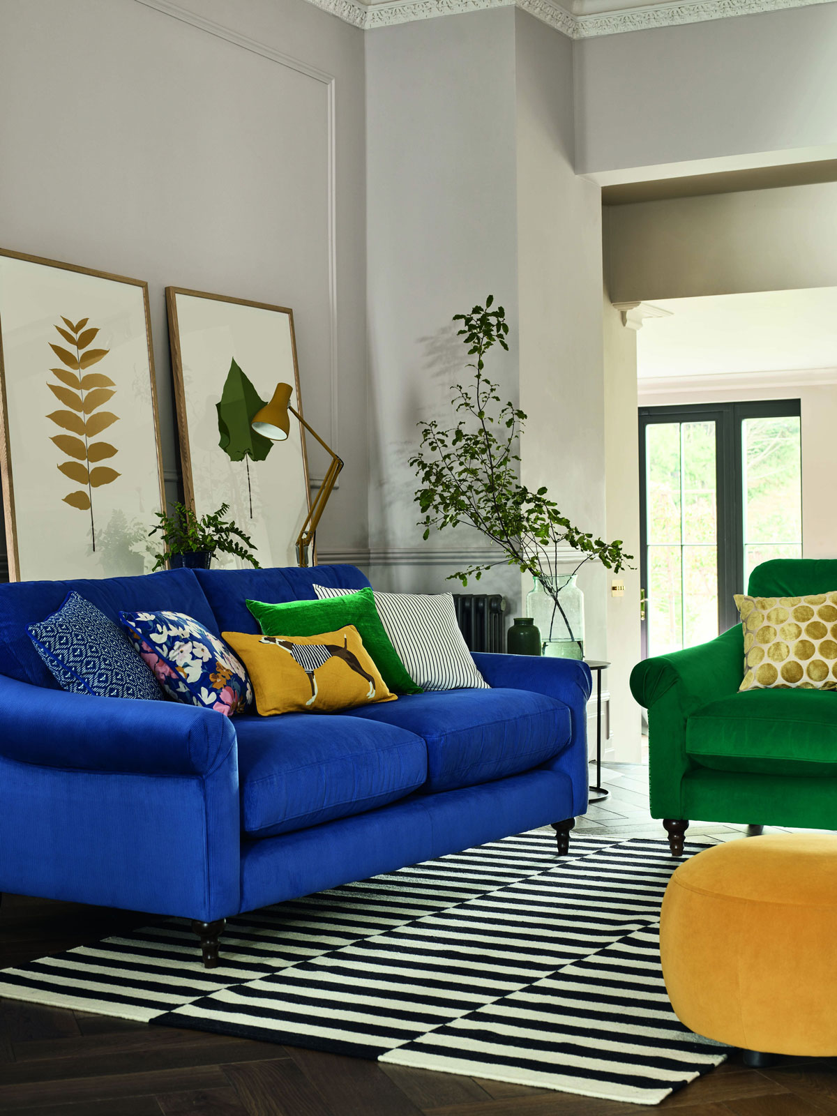 moderná obývačka s výraznou modrou sedačkou a výrazným zeleným kreslom a žltým taburetom, nábytok stojí na pásikavom čierno-bielom koberci