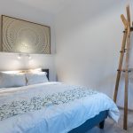spálňa s čalúnenou posteľou s bielymi obliečkami, po jednej strane steny sú umiestnené zamatové opierky na chrbát, nad posteľou visí obraz s mandalou