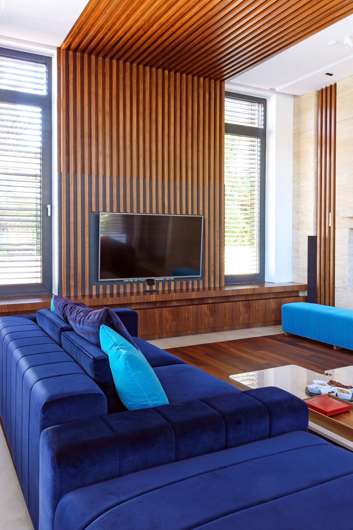 Elegantná obývačka s kráľovsky modrou sedačkou a lamelovým obkladom vedúcim od TV steny cez strop