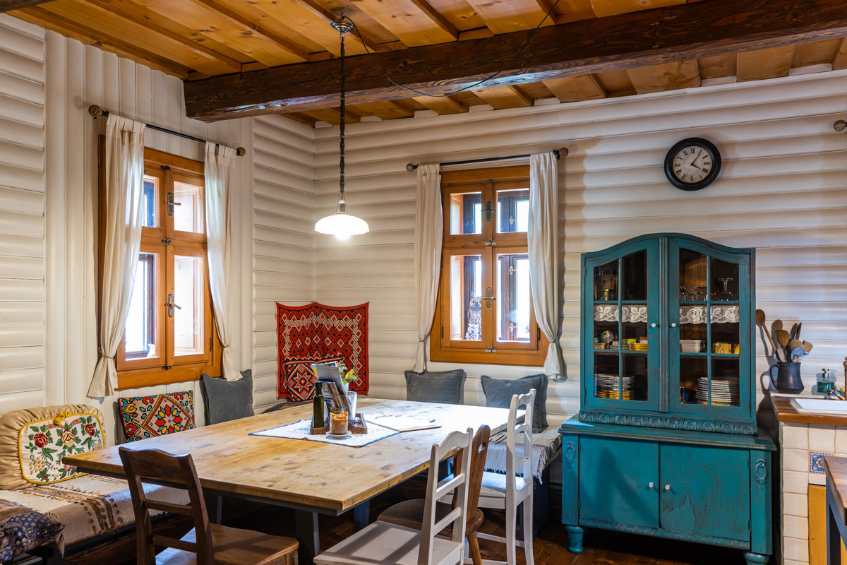 pohľad do jedálne v starej drevenici, v jednom rohu je rohová lavica, jedálenský stôl a stoličky, vedľa je starý zrepasovaný príborník v tyrkysovej farbe