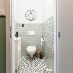 toaleta s WC, umývadlom, geometrickou retro dlažbou a sivým obkladom približne do polovice výšky stien