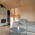 moderná obývačka so sivou sedačkou, celá miestnosť je obložená smrekovým drevom, v miestnosti je aj betónový krb