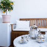 terasa bytu, v popredí mramorový stolík s čajovou porcelánovou súpravou, v pozadí je drevená lavica a citrónovník