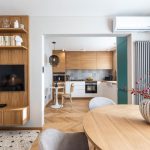 pohľad do interiéru bytu ladeného v neutrálnych farbách a dubovom dekore, z obývačky s jedálenským stolom sa prechádza otvoreným priechodom bez dverí do kuchyne