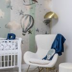 detail detskej izby s bielym kreslom so zlatou podnožou a bielou postieľkou, za kreslom stojí zlatá lampa a na stene vidieť tapetu so vzorom balónov a lietadla