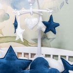 detail detskej postieľky s vankúšmi v tvare hviezd a obláčikov a kolotočom s hviezdičkami a srdiečkami