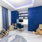 detská izba pre chlapca s pracovným kútikom s modrými skriňami a pracovným stolom, podlaha je z mramoru a nechýba na nej ani koberec s detským motívom