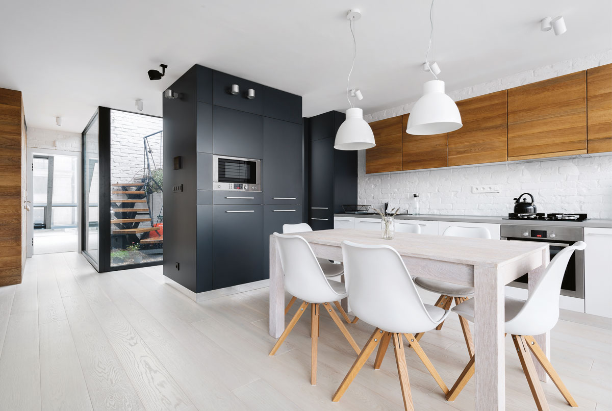 pohľad na modernú kuchyňu s jedálenským stolom, minimalistickou kuchynskou linkou a vstavanými spotrebičmi, z kuchyne je výhľad do chodby s preskleným átriom