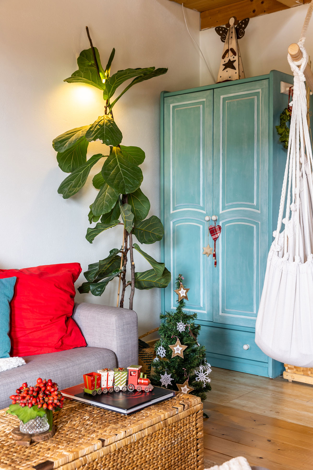 obývačka so zrenovovanou skriňou, malým vianočným stromčekom, sivou sedačkou a prúteným košom, ktorý slúži ako konferenčný stolík