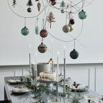 Moderne prestretý vianočný stôl s ihličnatými vetvičkami, nad stolom visí dekorácia s vianočnými ozdobami