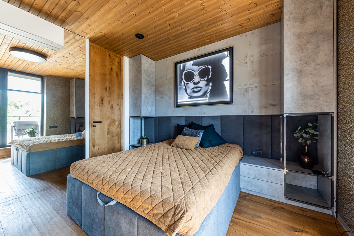 spálňa s čalúnenou posteľou vsadená do vstavaných skriniek z pohľadového betónu, na strope je drevený obklad, súčasťou spálne je aj kúpeľňa