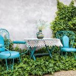 oddychový kútik v záhrade s tyrkysovými dekoratívnymi stoličkami a stolíkom, vsadené sú do porastu z brečtanu