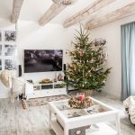 Sviatočná obývačka v bielej farbe, s vianočným živým stromčekom a hojdačkou visiacou z trámov