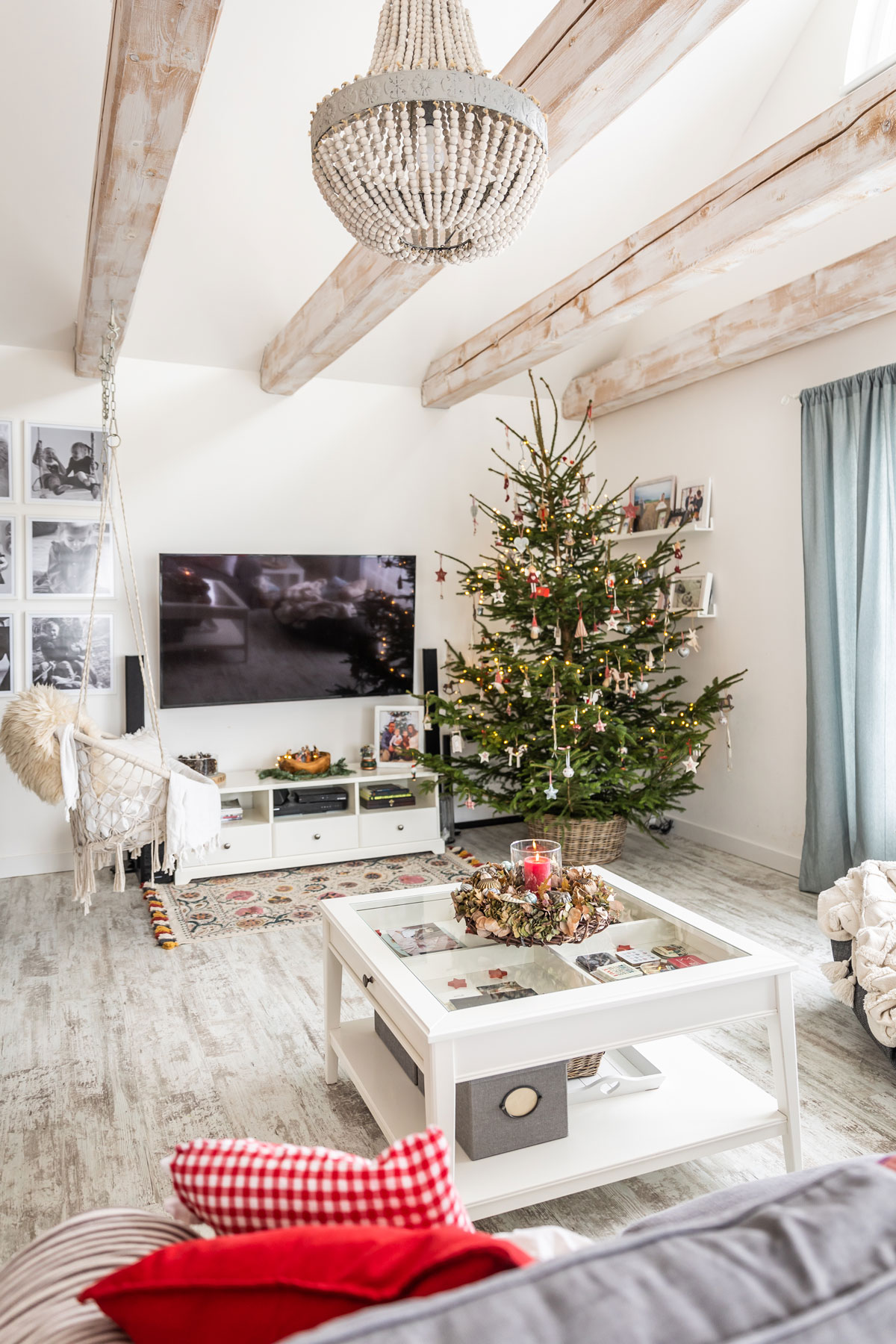 Sviatočná obývačka v bielej farbe, s vianočným živým stromčekom a hojdačkou visiacou z trámov