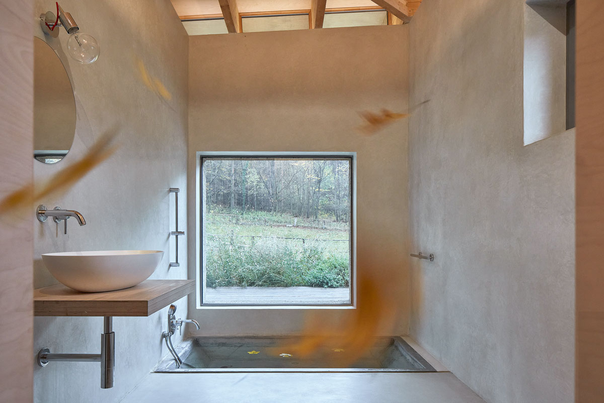 minimalistická kúpeľňa s veľkým oknom vedľa betónovej vane zapustenej do podlahy