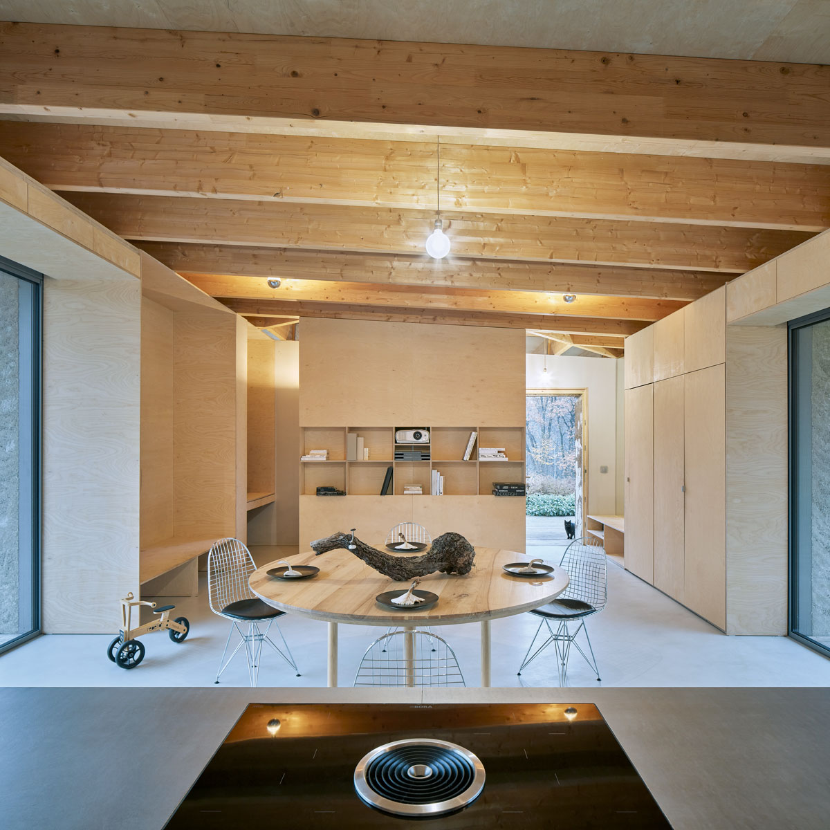 denný priestor v modernom minimalistickom rodinnom dome s dreveným jedálenským stolom a kovovými stoličkami, v pozadí je stena s úložnými priestormi