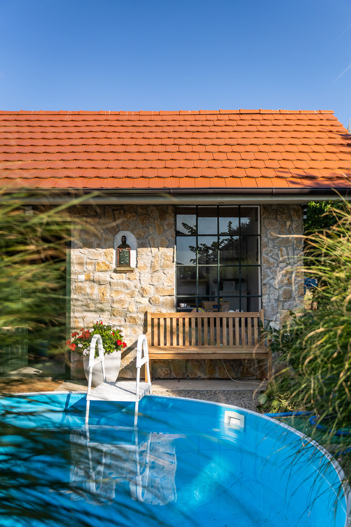 záhradný domček vo vidieckom štýle s veľkými oknami a fasádou obloženou kameňom, pred domčekom je bazén