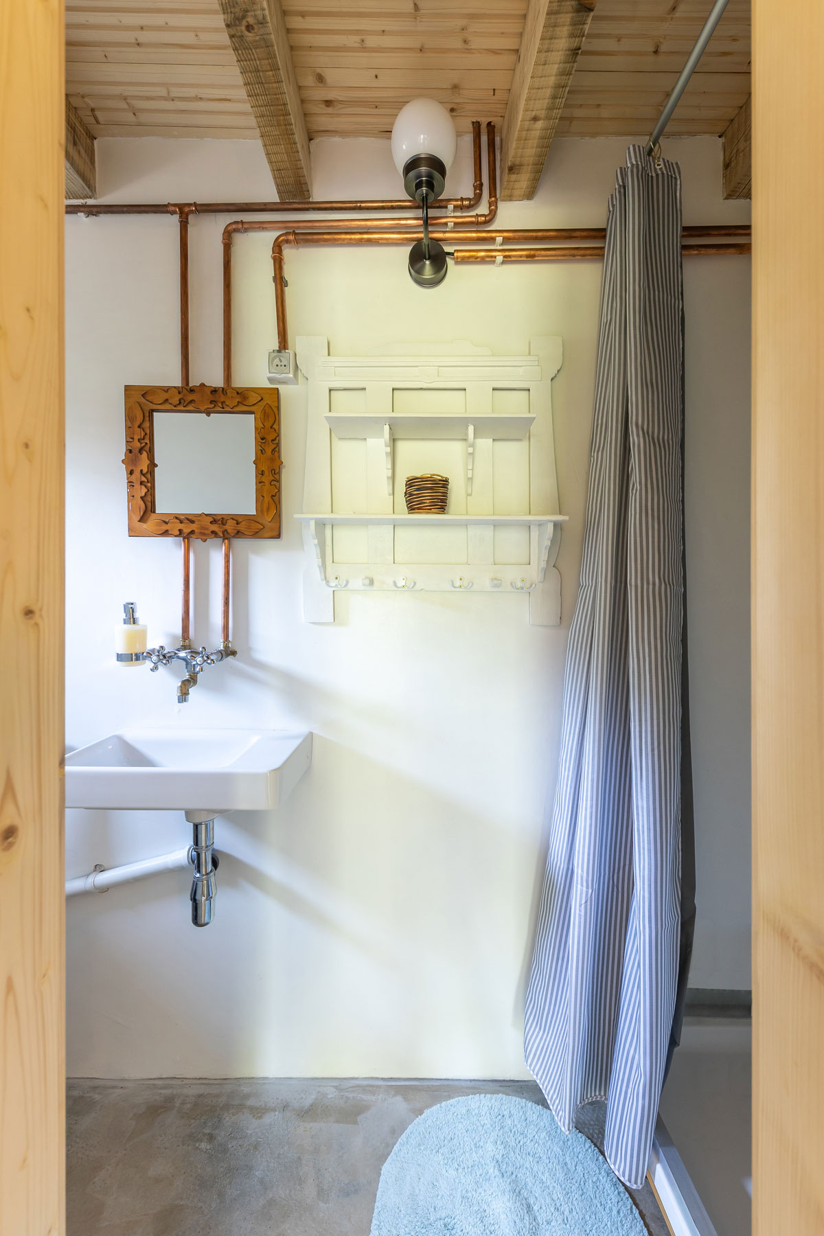 jednoduchá kúpeľňa v záhradnej chatke s betónovou podlahou, na stene sú priznané medené vodovodné rúrky