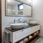 moderne ladená kúpeľňa s bielou závesnou skrinkou s dvoma umývadlami, nad nimi visí zrkadlo v striebornom glamour ráme