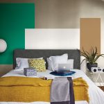 Spálňa s čalúnenou posteľou, za ňou je stena s farebnými geometrickými tvarmi