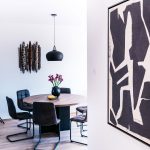 jedáleň s okrúhlym stolom a čalúnenými stoličkami na kovových nohách, na stene visí abstraktný geometrický obraz
