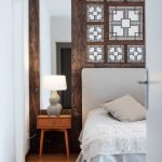 neutrálne ladená spálňa v modernom rustikálnom štýle, za posteľou je drevený obklad s vyrezávaným ornamentom