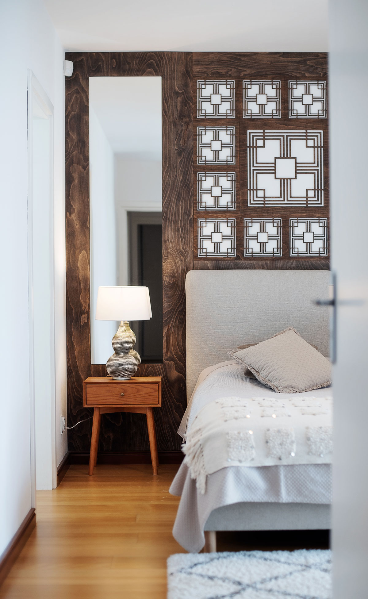 neutrálne ladená spálňa v modernom rustikálnom štýle, za posteľou je drevený obklad s vyrezávaným ornamentom