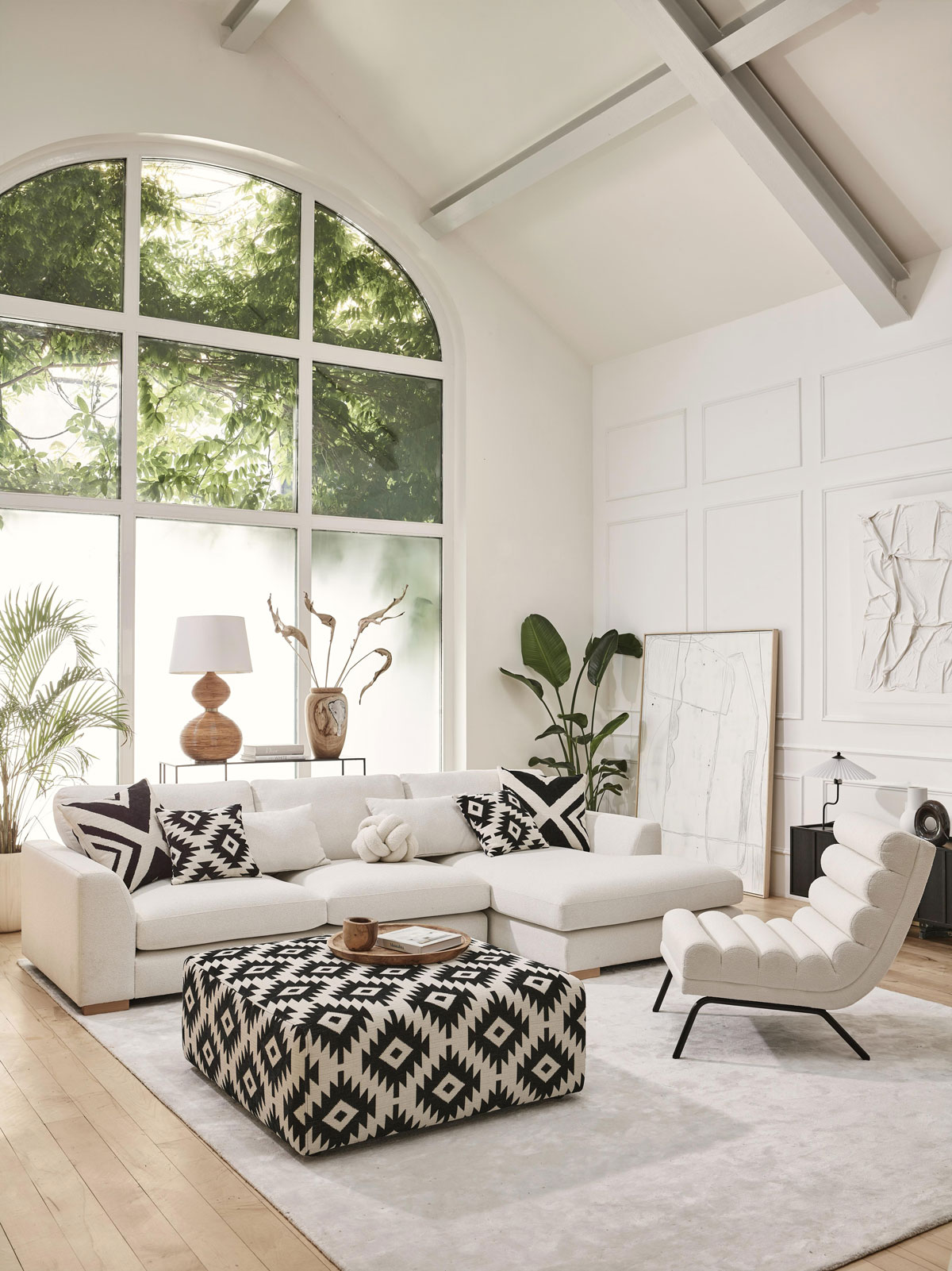 moderná obývačka v bielej farbe s jednoduchou sedačkou do L a vzorovaným čiernobielym veľkým taburetom