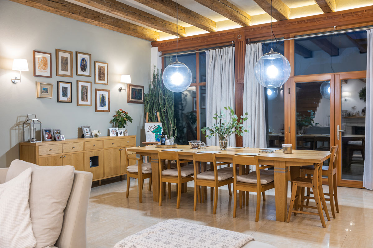 jedáleň v rodinnom dome s presklenou stenou do záhrady, na strope sú pôvodné podsvietené drevené trámy