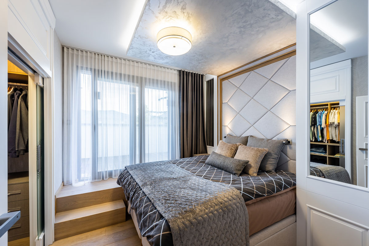 elegantná spálňa s polstrovanou zástenou za posteľou, posteľ je pod úrovňou vonkajšej terasy, na ktorú vedú schodíky popri posteli