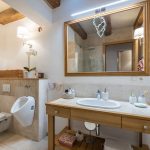 spojená kúpeľňa a toaleta s neutrálnym hnedým obkladom, drevený, stolíkom s umývadlom, zrkadlom v drevenom ráme a stropnými trámami