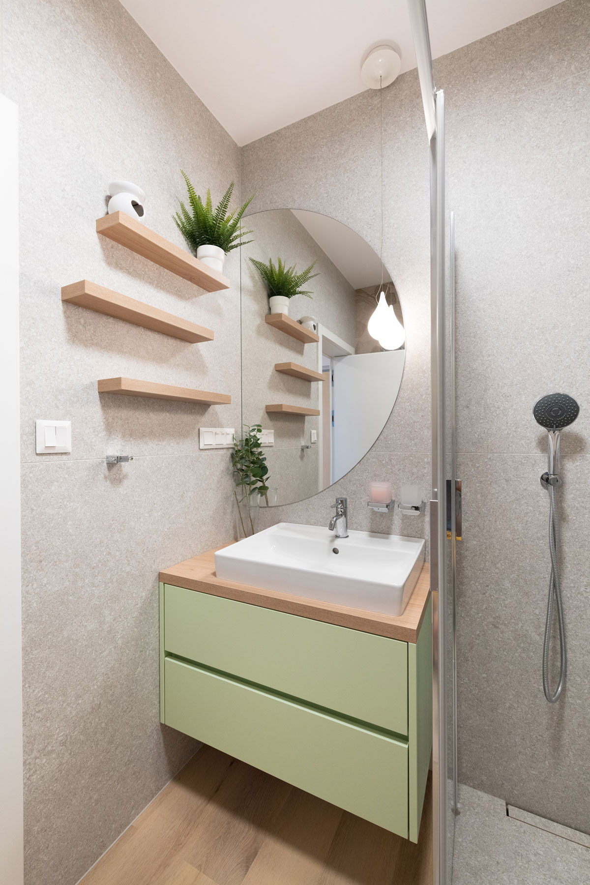kúpeľňa so sivým obkladom, jednoduchými dubovými policami a pastelovou zelenou umývadlovou skrinkou