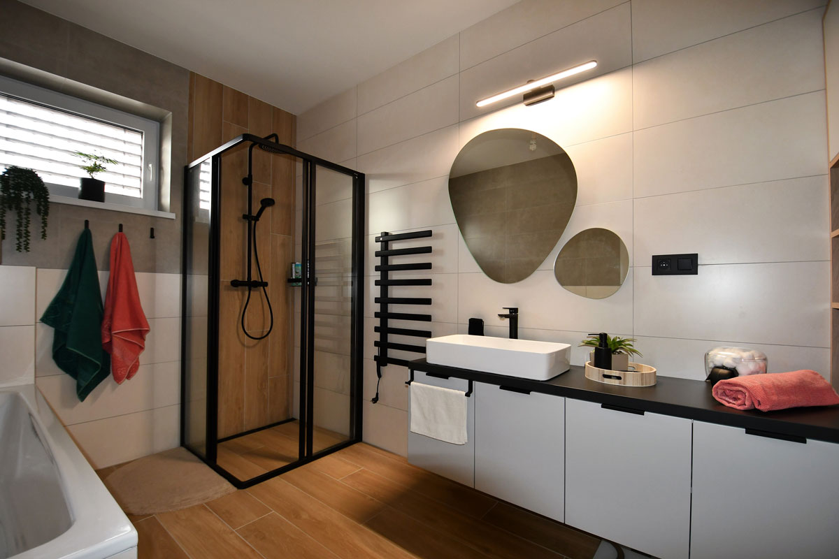 moderná priestranná kúpeľňa v bielej farbe s čiernymi detailmi, nad umývadlovými skrinkami visia dve zrkadlá nepravidelných tvarov