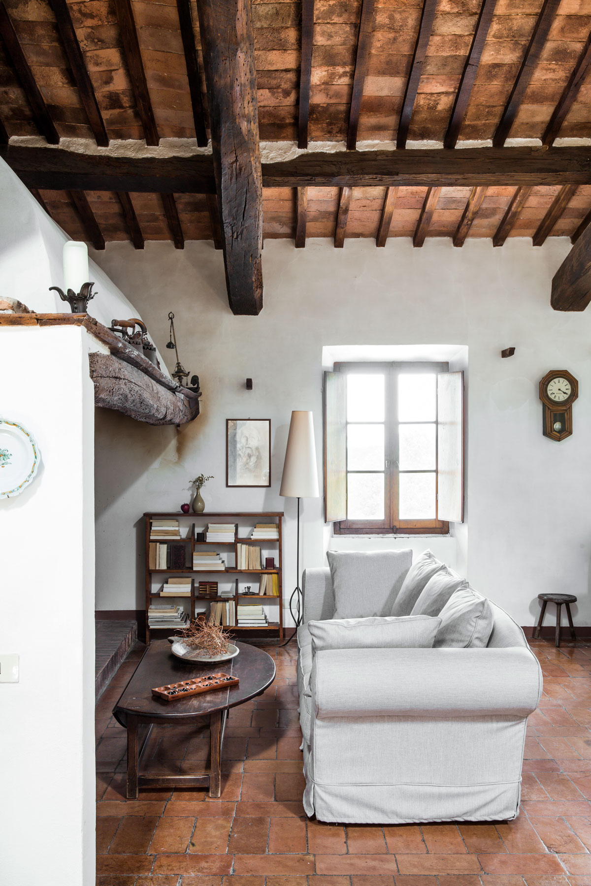 vidiecka obývačka v Toskánsku s kamennou podlahou a bielou sedačkou, jednoduchý rustikálny štýl dopĺňajú drevené stropné trámy