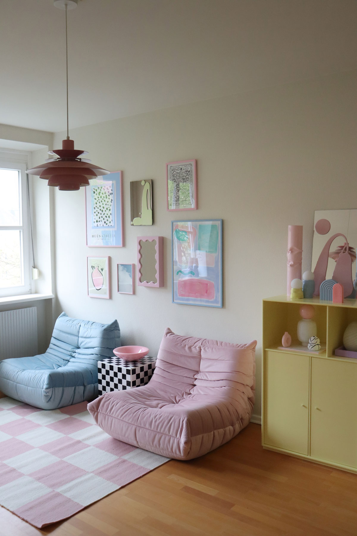 pastelová obývačka s dvoma kreslami v ružovej a modrej farbe, šachovnicovým stolíkom a pastelovou žltou skriňou s veselými dekoráciami