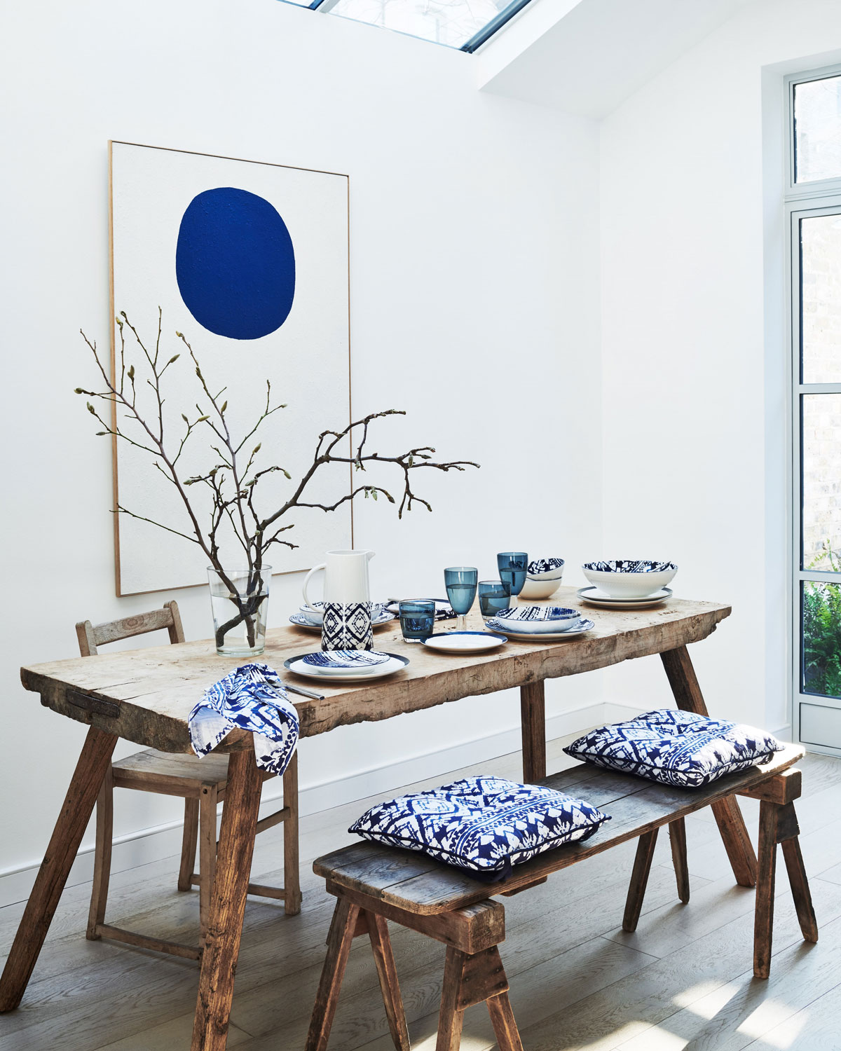 Rustikálny drevený stôl s lavicou s modrými podsedákmi a obrazom s modrým kruhom