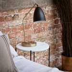 Nočný stolík s kovovou zlatou lampou pri tehlovej stene v spálni